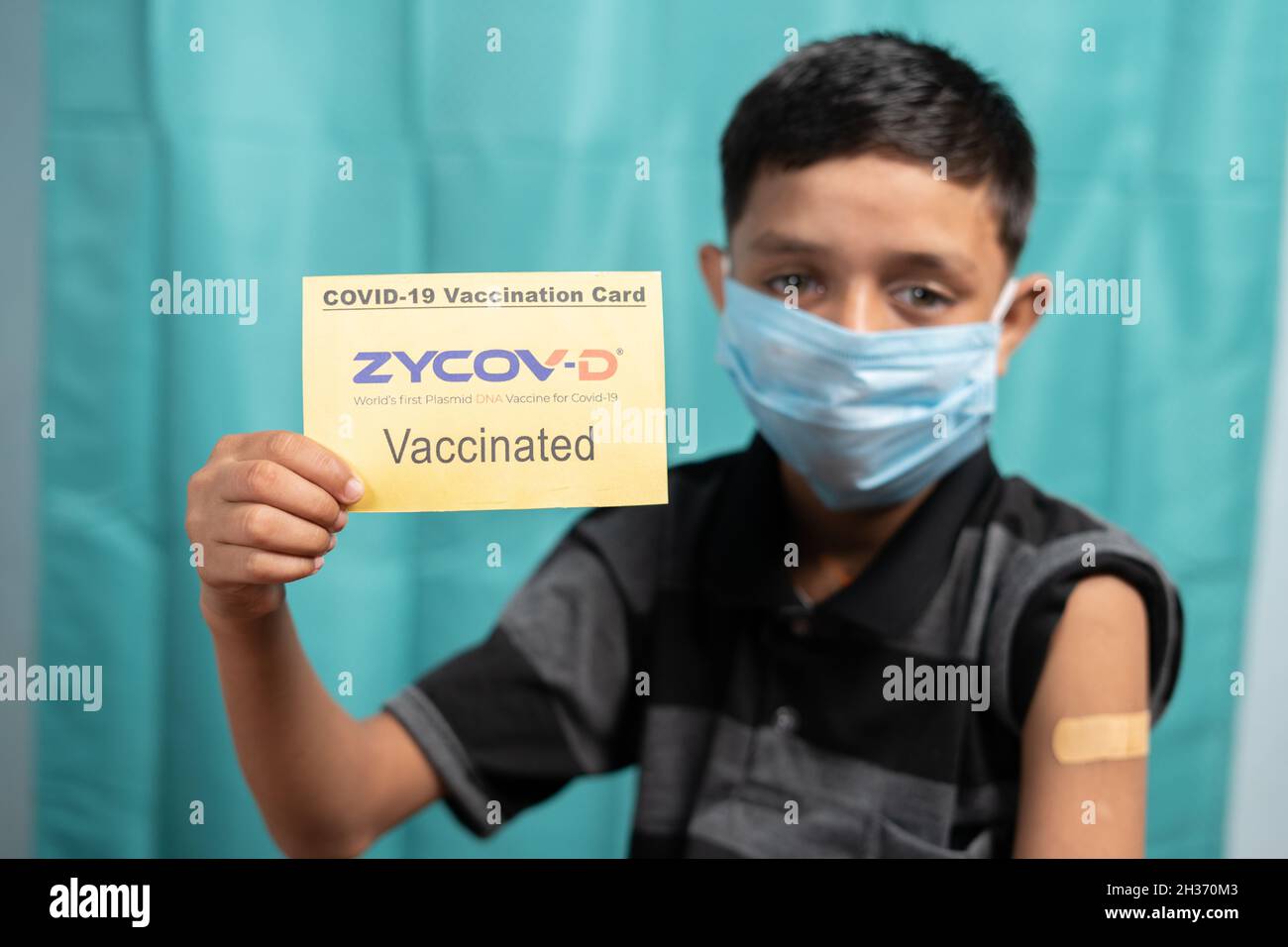 Maski, India - October 26, 2021 : Young kid with medical face mask showing ZYCOV-D Covid-19 or coronavirus Vaccinated report card. Stock Photo