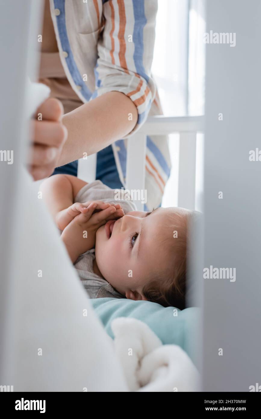 Smiling kid with down syndrome lying in baby crib near mother Stock