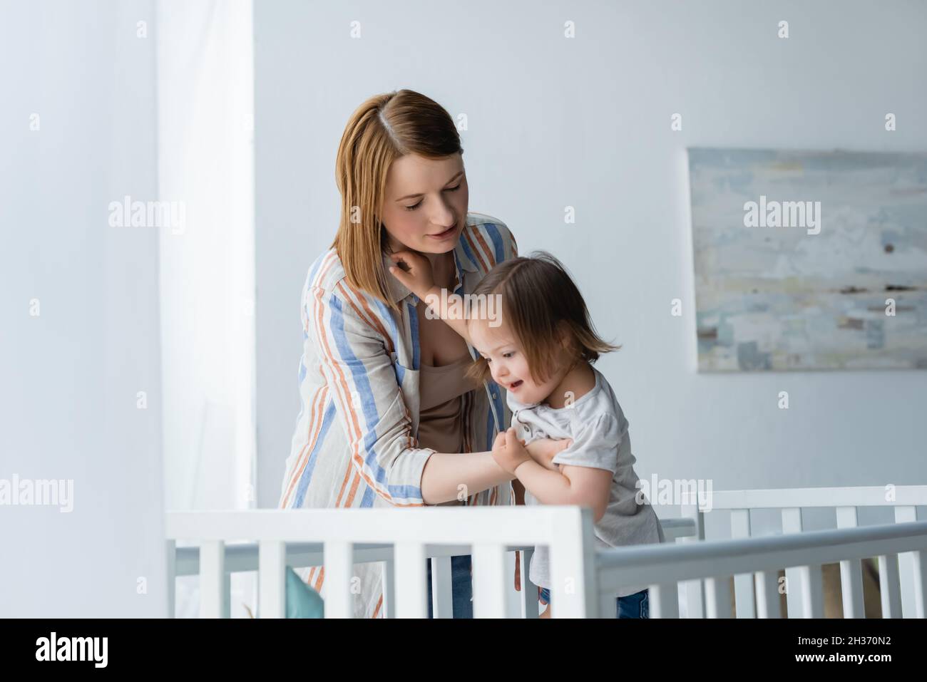 Mother holding baby with down syndrome near crib at home Stock Photo