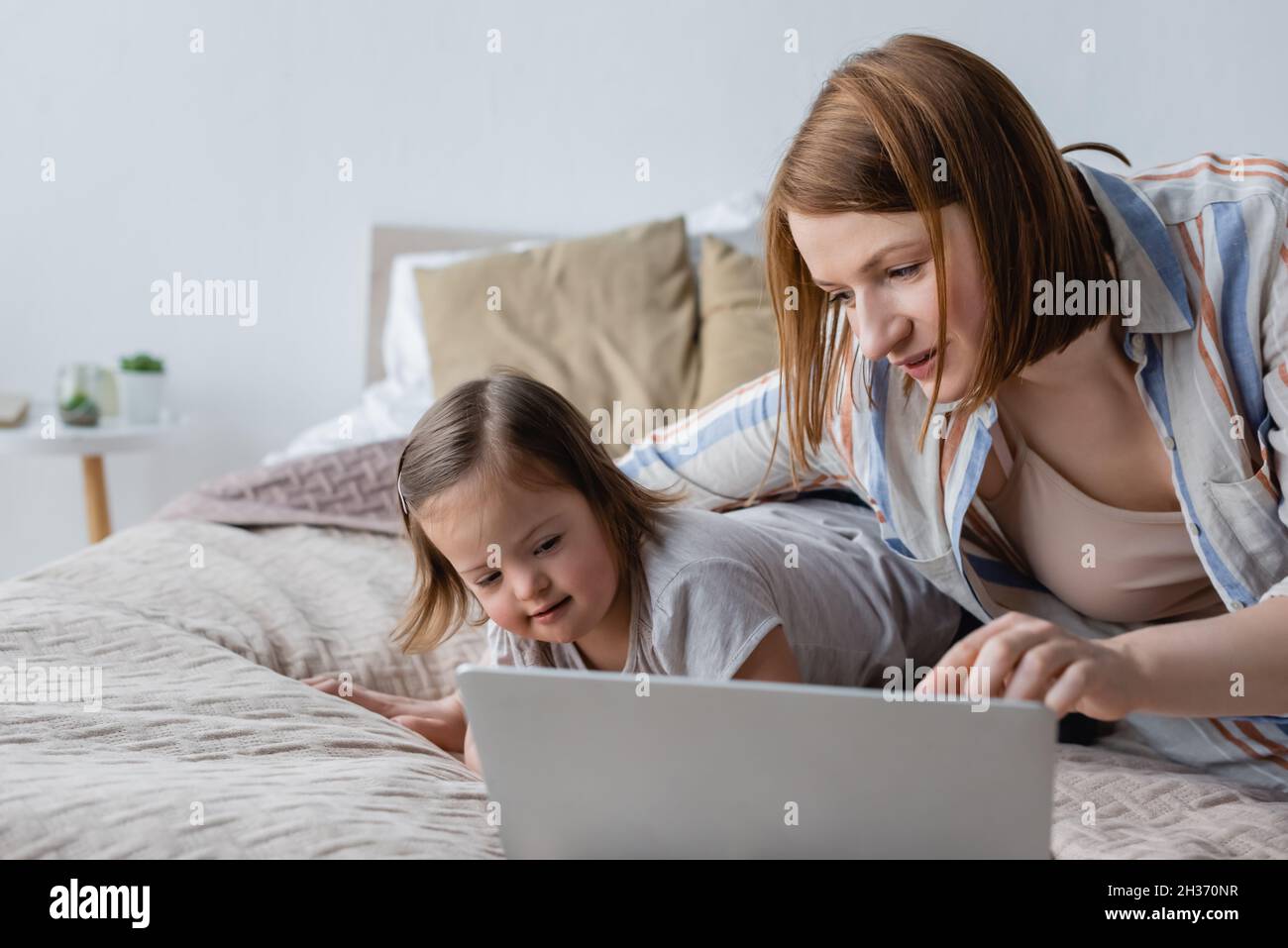 Freelancer using laptop near daughter with down syndrome on bed Stock Photo