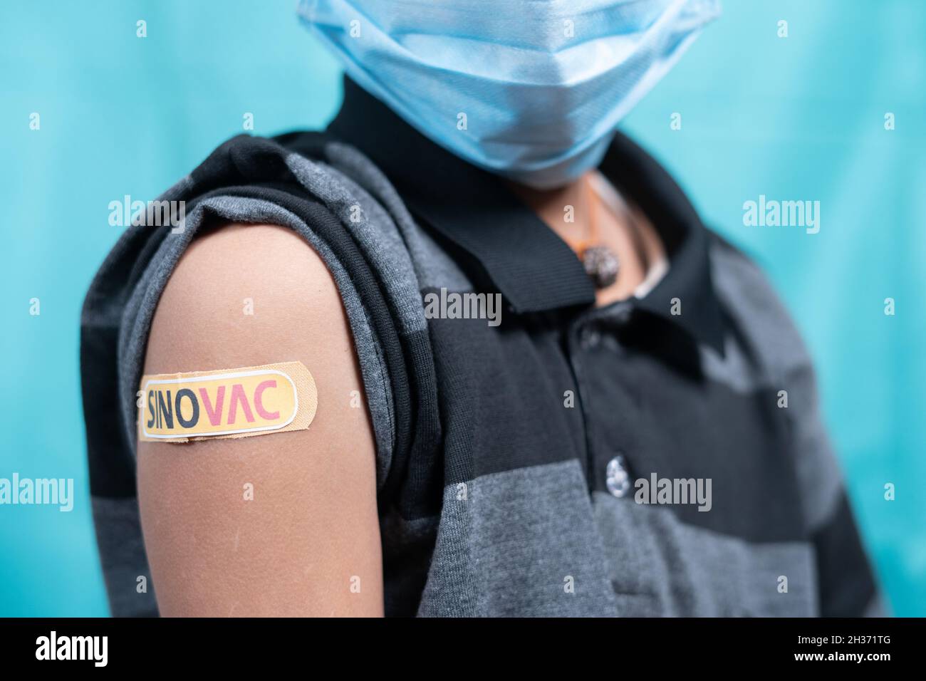 Maski, India - October 26, 2021 : kid with medical face mask showing Sinovac vaccine bandage on shoulder, Coronavirus or covid vaccination for Stock Photo