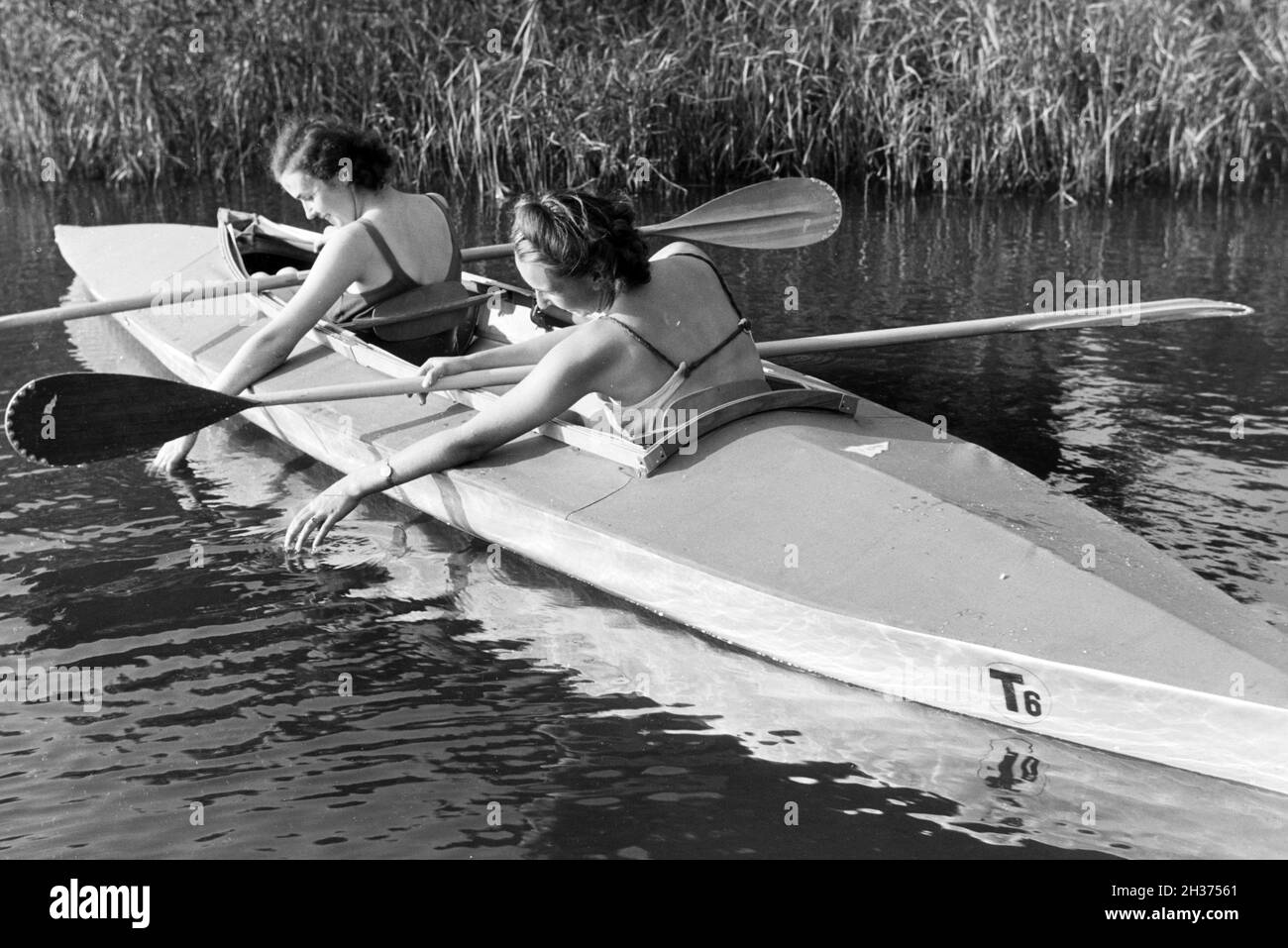 Zwei junge Frauen in Badeanzügen paddeln in einem Boot / Klepper T6 auf dem See, Deutschland 1930er Jahre. Two young women in bathing suits are paddling in a boat / Klepper T6 on a lake, Germany 1930s. Stock Photo