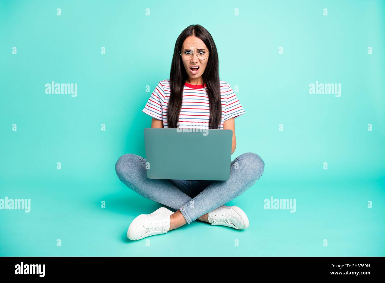 Full size photo of impressed displeased girl sit on floor use laptop open mouth isolated on teal color background Stock Photo
