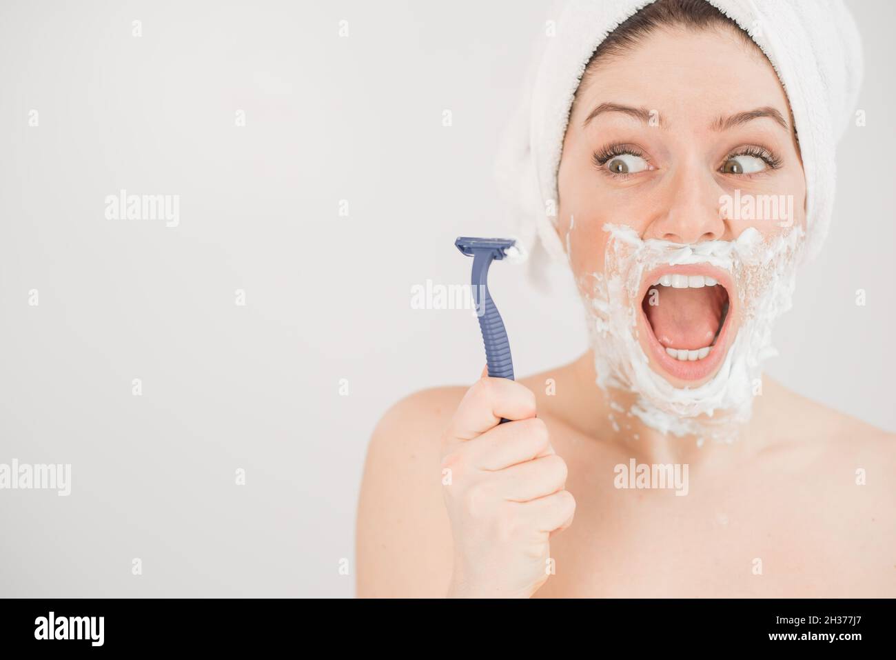 Funny portrait of a woman with shaving foam on her face holding a razor
