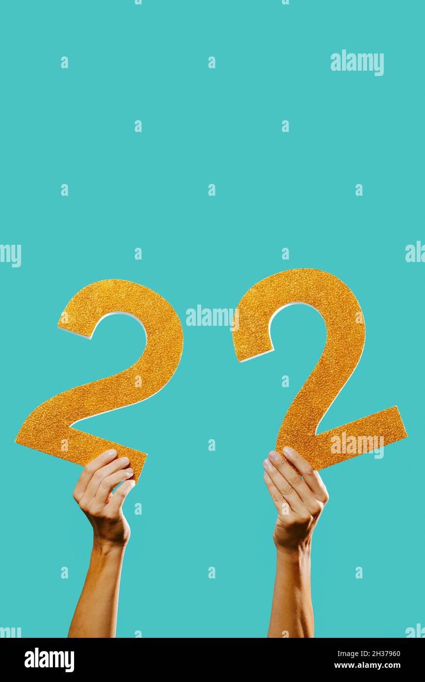 closeup of a man holding two golden three-dimensional numbers forming the number 22 on a blue background, with some blank space on top Stock Photo