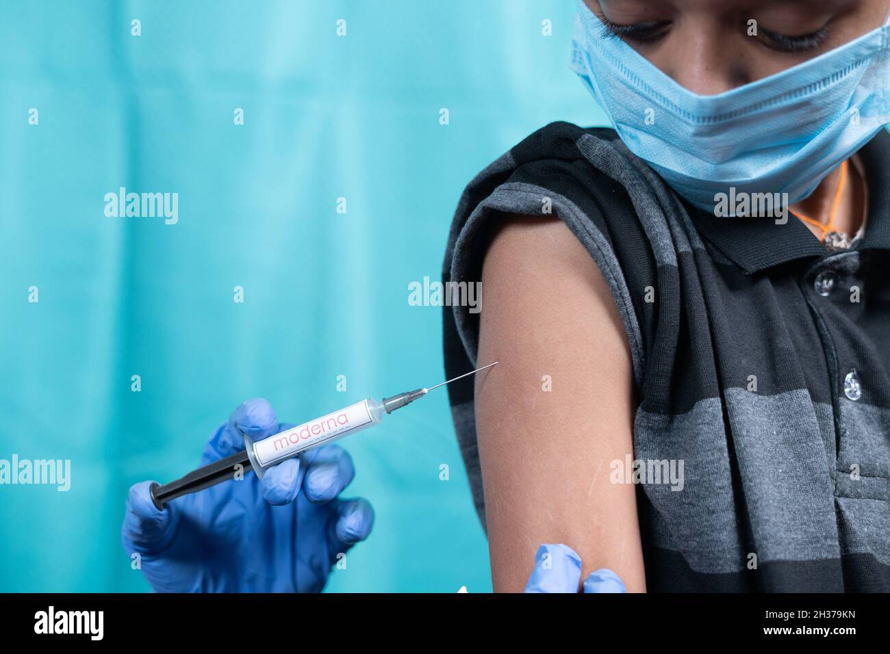 Maski, India - October 26, 2021 : Young kid with medical face mask getting vaccinated Moderna Covid-19 or coronavirus children vaccine. Stock Photo