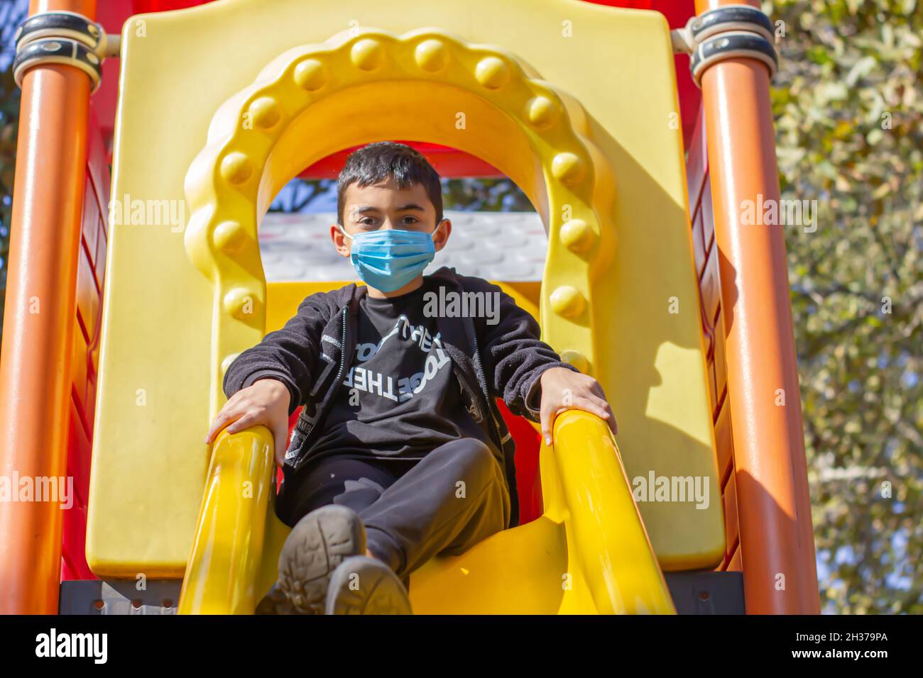 Masked boy in the park. Brunette boy in black hoodie and blue mask plays in the park. Front view. Selective focus Stock Photo