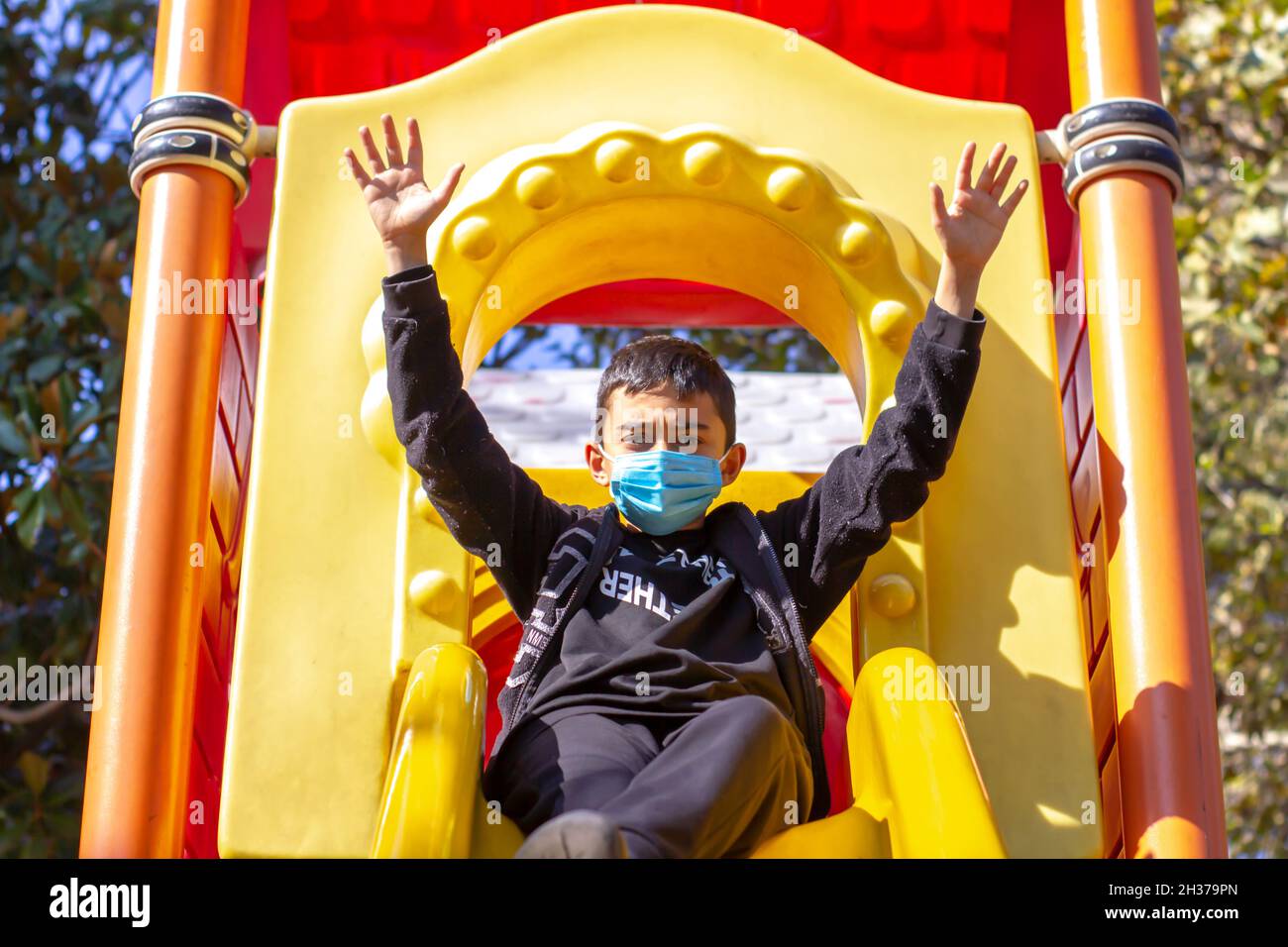 Masked boy in the park. Brunette boy in black hoodie and blue mask raised hands. Front view. selective focus Stock Photo