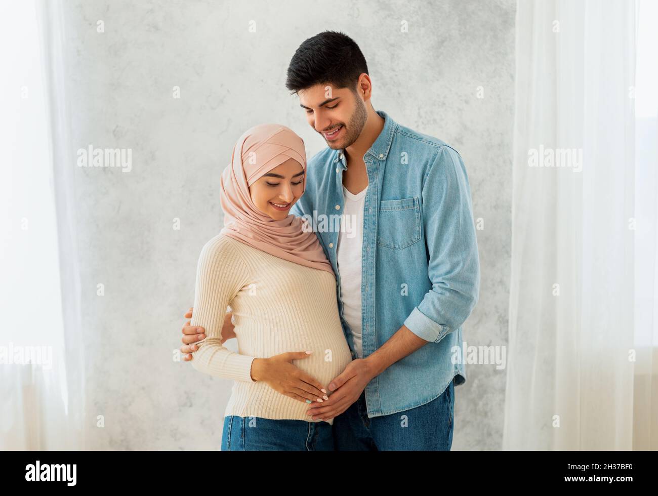 Parenthood concept. Loving arab pregnant woman and her husband embracing, smiling and touching belly Stock Photo