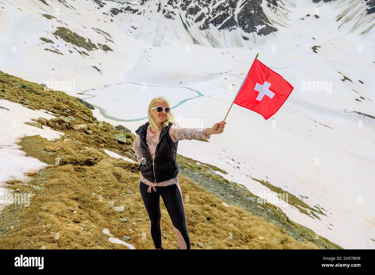 Tourist woman at with swiss flag in the snow on top of Muottas Muragl mount of Switzerland. Popular mountain excursions at Lej Muragl in Graubunden Stock Photo