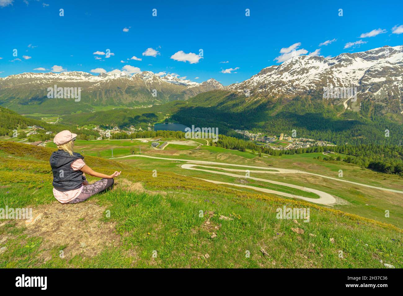 Woman doing yoga lotus pose on top of Piz Nair in Switzerland. Yoga meditation by Lake St. Moritz and Silvaplana skyline in Grisons Canton of Stock Photo