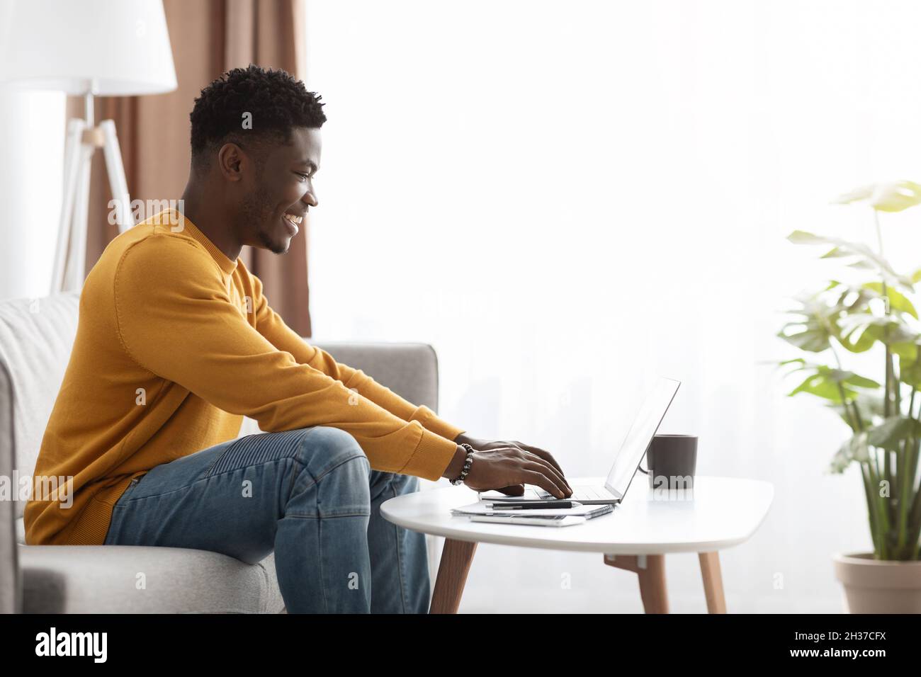 Black man freelancer sitting on couch at home, using laptop Stock Photo