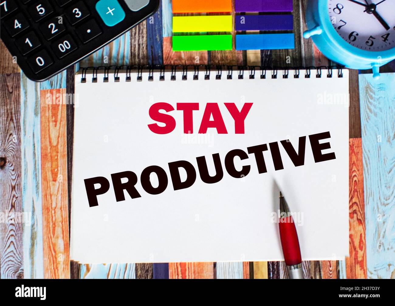 Text Stay productive written on a notepad in the office with surroundings such as a calculator, sticky notes, alarm clock and pen. Stock Photo