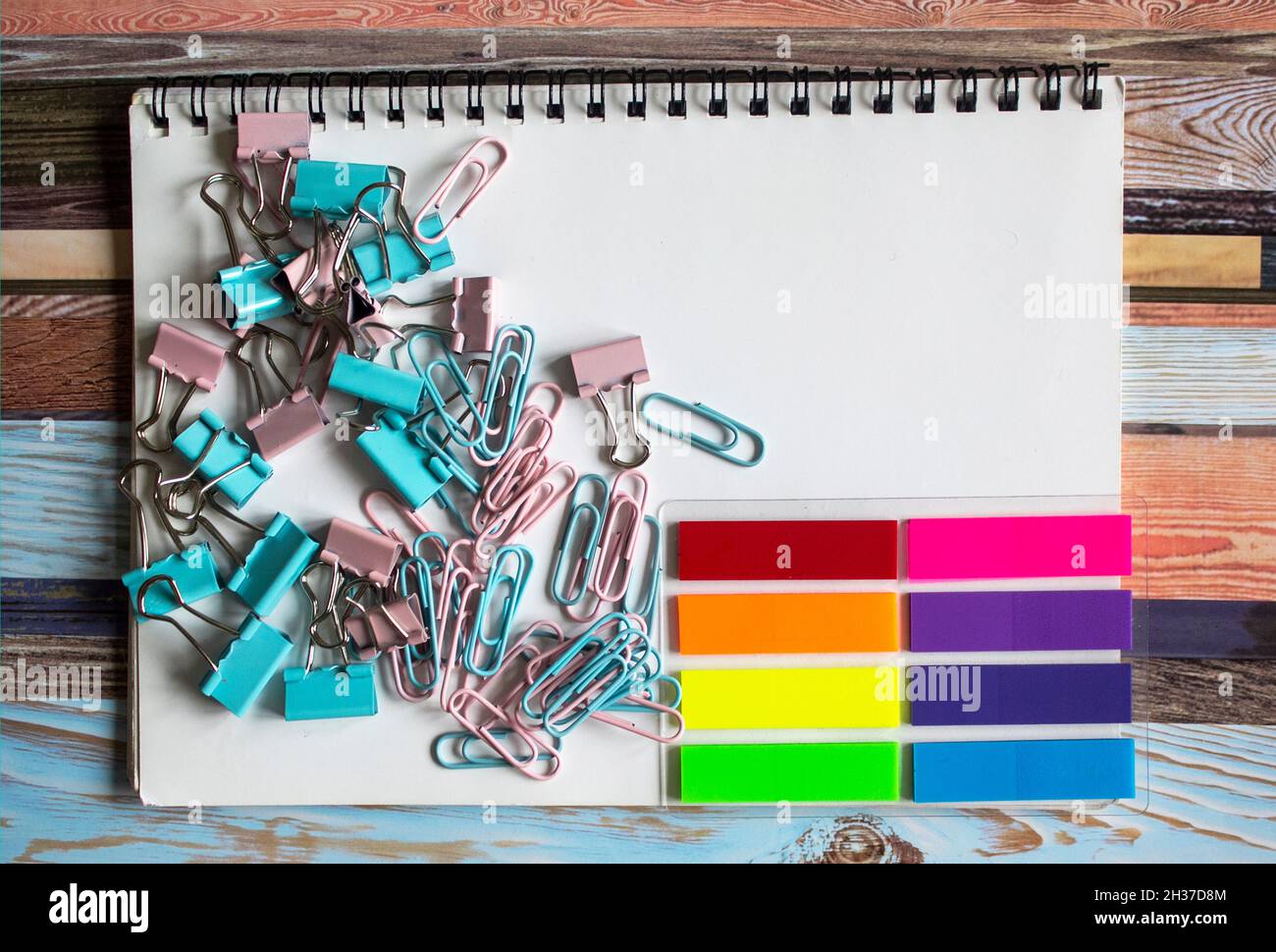 Collection of different types of paper clips on a white notepad and 