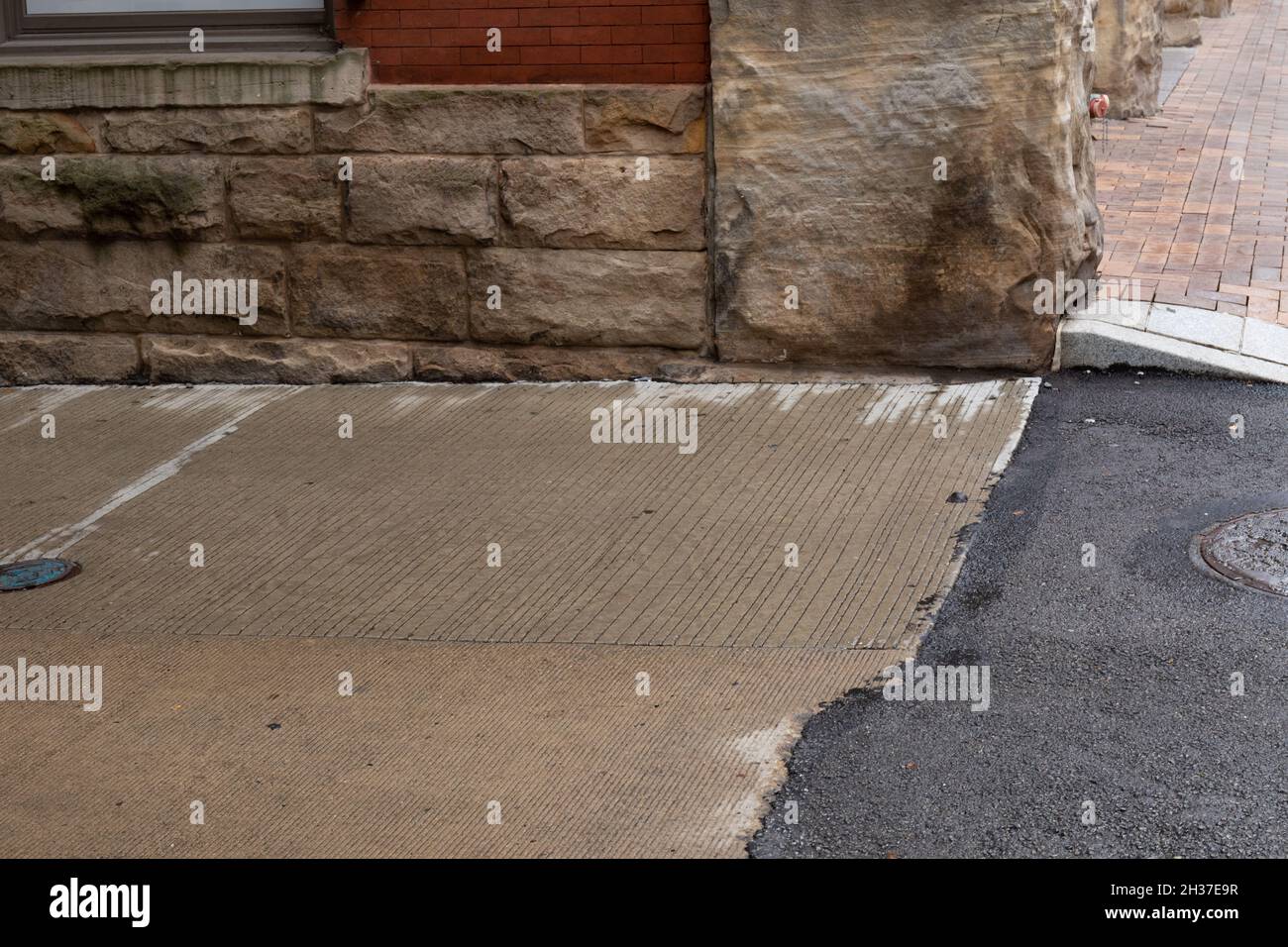 Corner of a red brick and rusticated stone building meeting a brick sidewalk, concrete driveway, and asphalt road surface, horizontal aspect Stock Photo