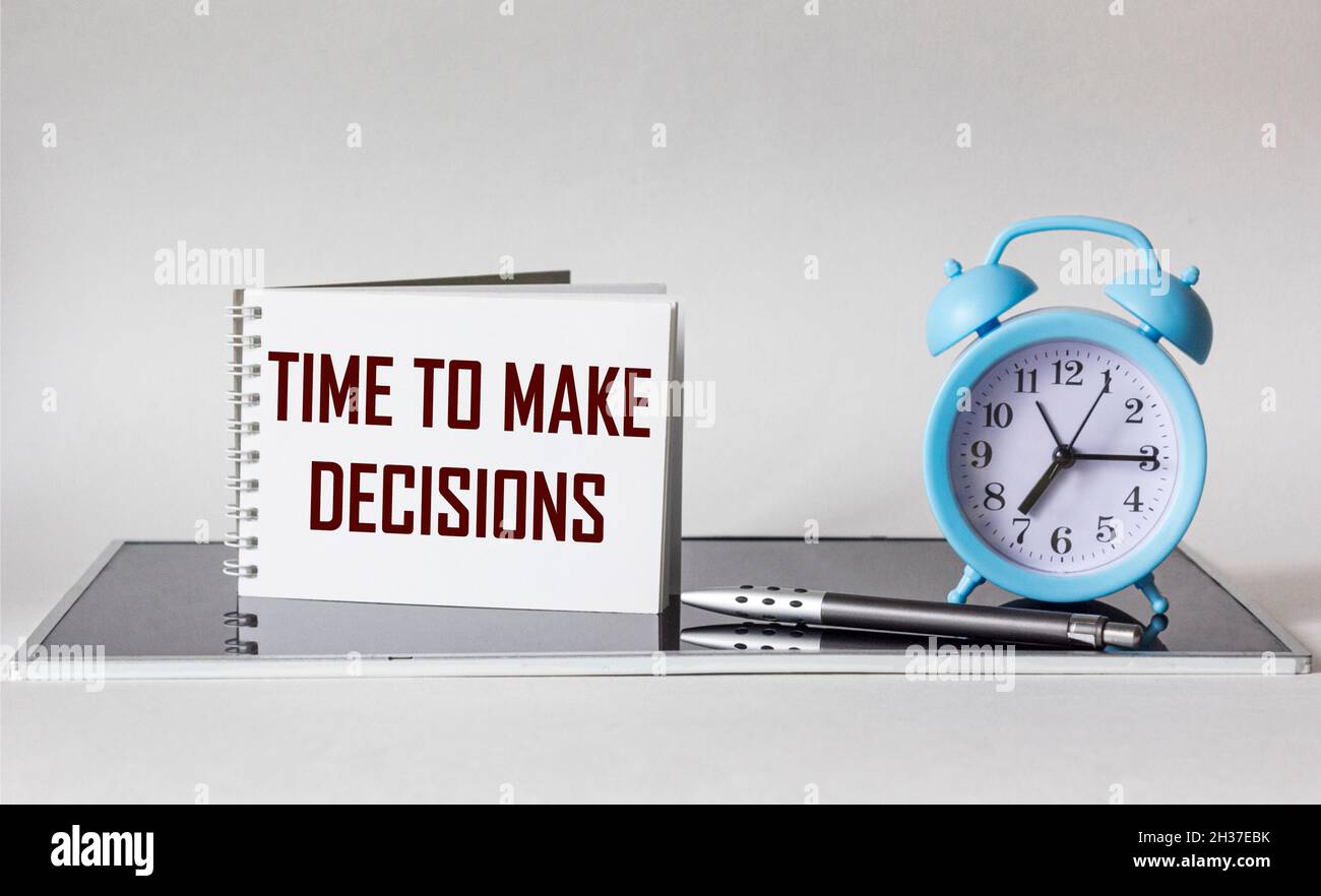 TIME TO MAKE DECISIONS text to write on a notebook .There is a clock and a pen on a white and black background. Stock Photo
