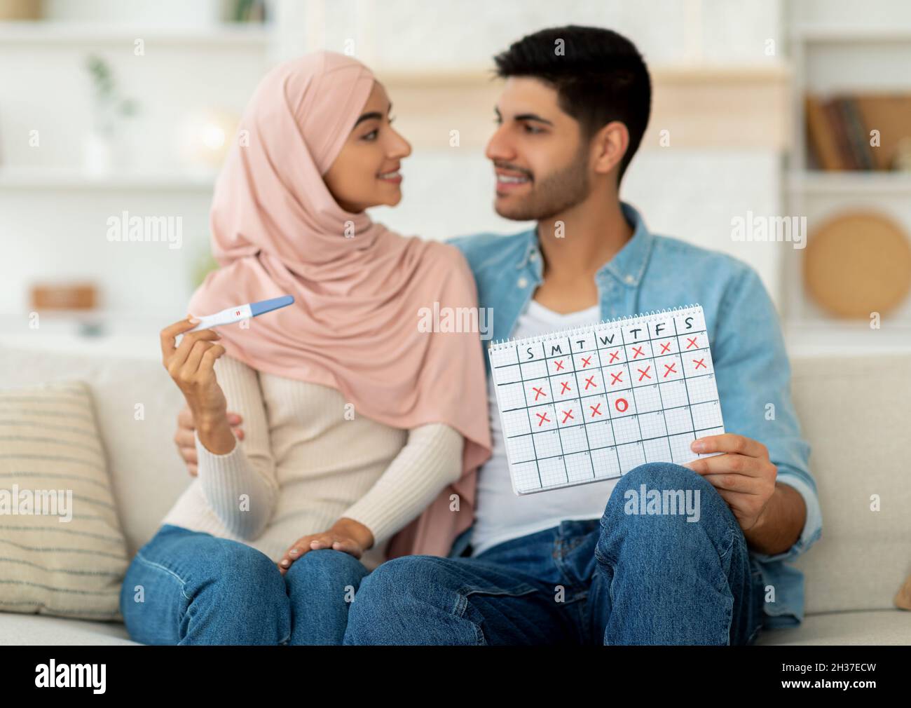 Planning pregnancy and expecting baby concept. Pretty arab couple holding positive pregnancy test and ovulation calendar Stock Photo