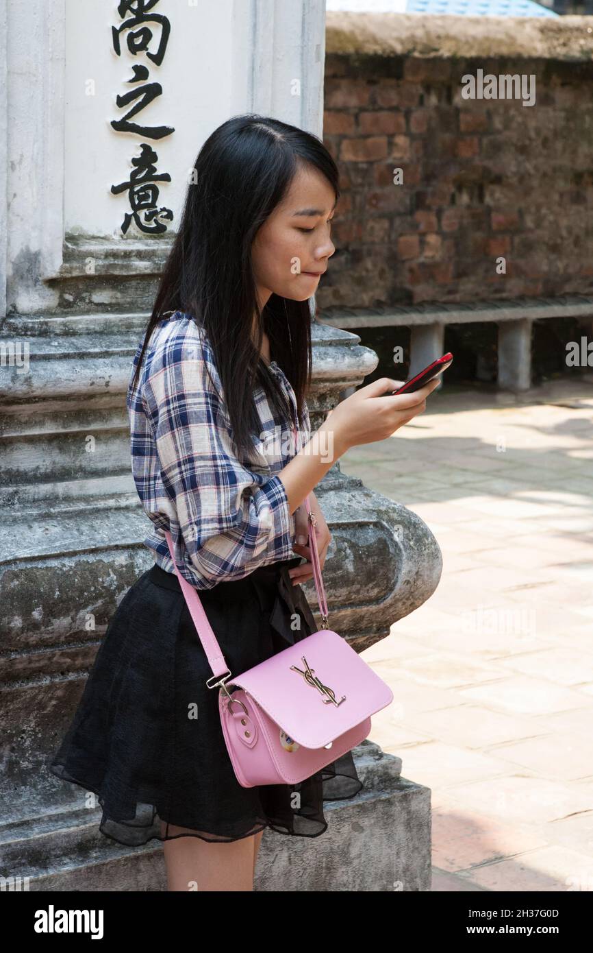 Young female visitor to the Temple of Literature (Văn Miếu), looking at her mobile 'phone: Hanoi, Viet Nam Stock Photo