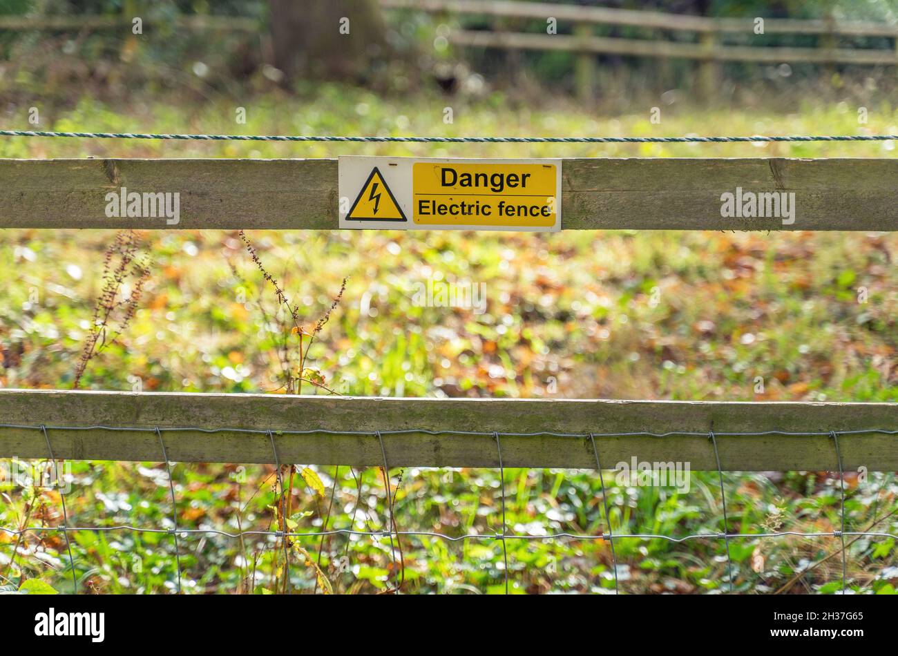 Yellow danger electric fence sign on a wooden and metal fence Stock