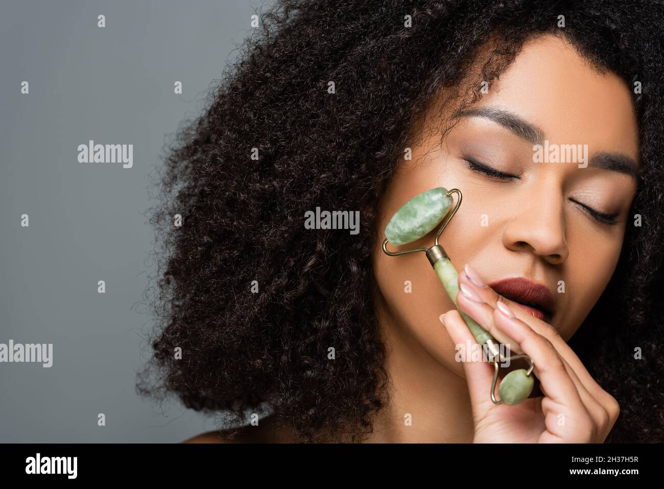 african american woman with perfect skin massaging face with jade ...