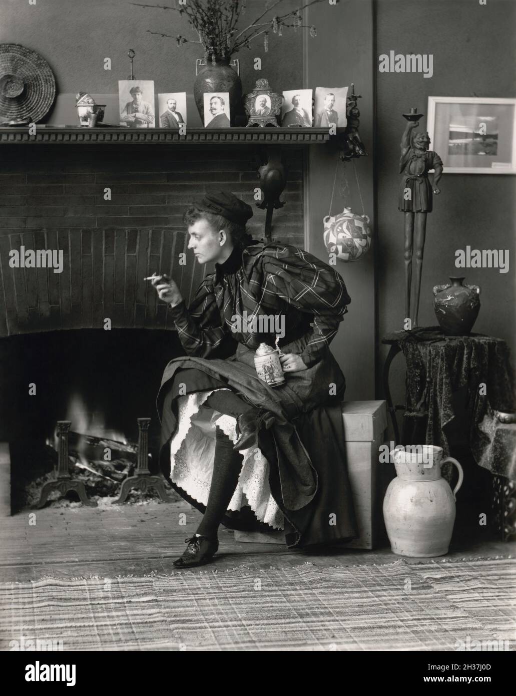 Frances Benjamin Johnston- Self Portrait as New Woman seated in front of fireplace, holding cigarette in one hand and a beer stein in the other hand. Stock Photo
