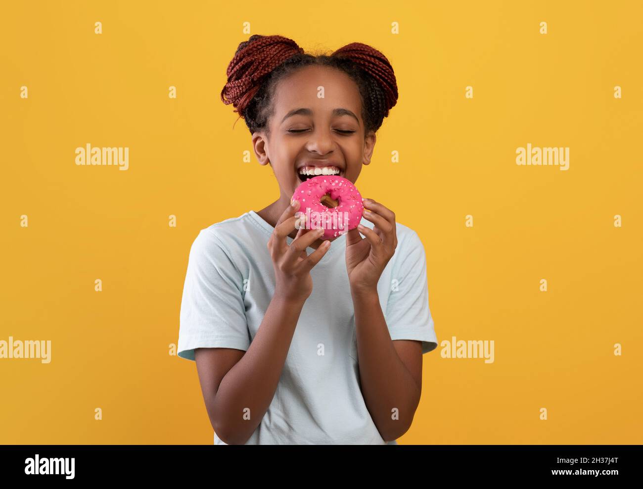 Sweet tooth black girl eating donut on yellow Stock Photo