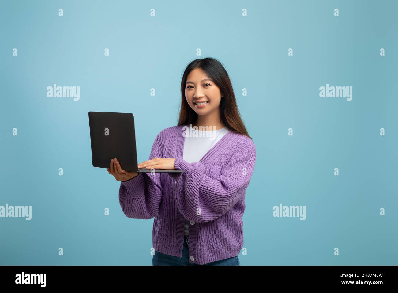 Portrait of happy young asian lady holding and using laptop over blue ...
