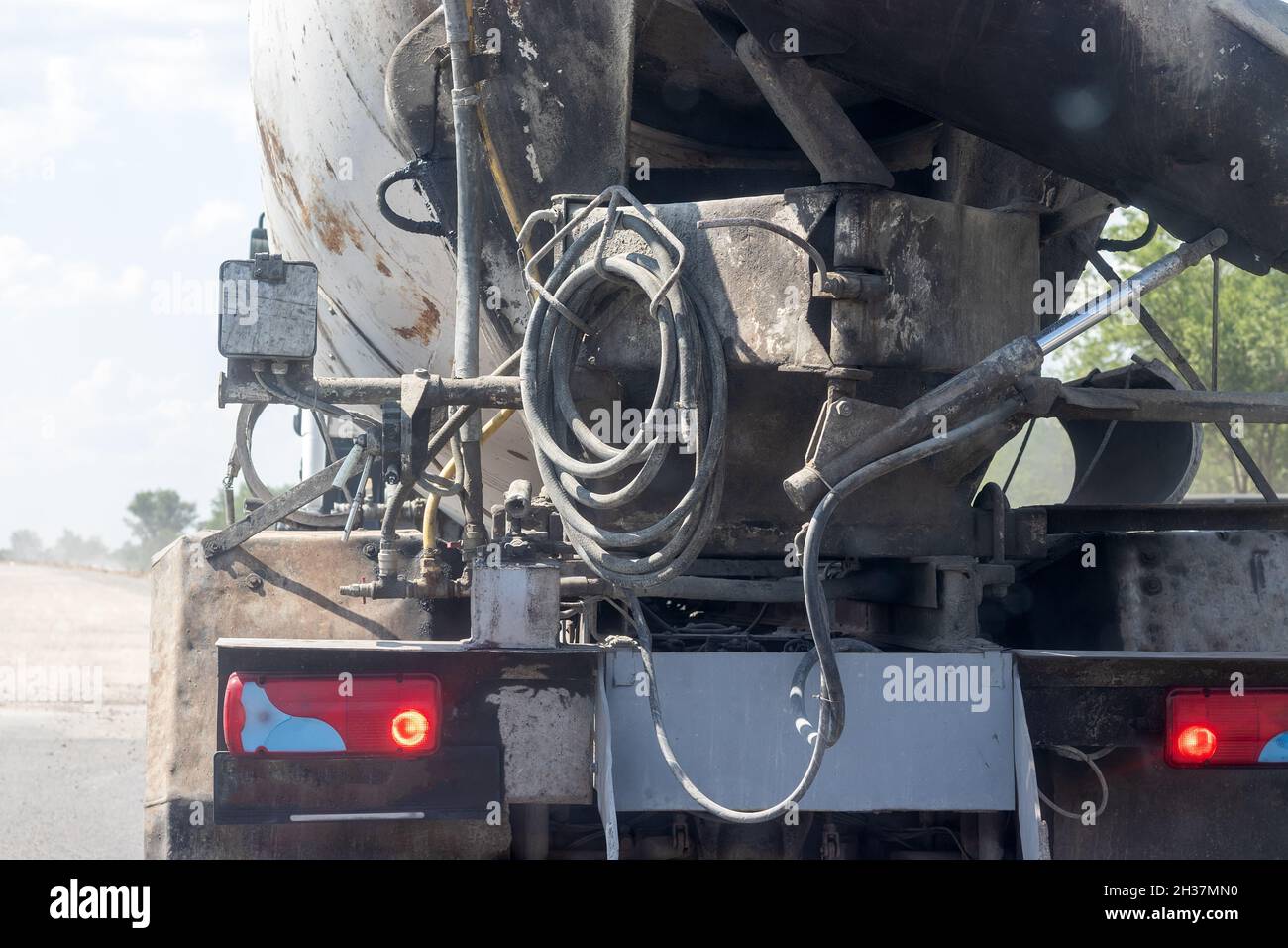 Concrete mixer truck rear view with hoses and burning taillights during