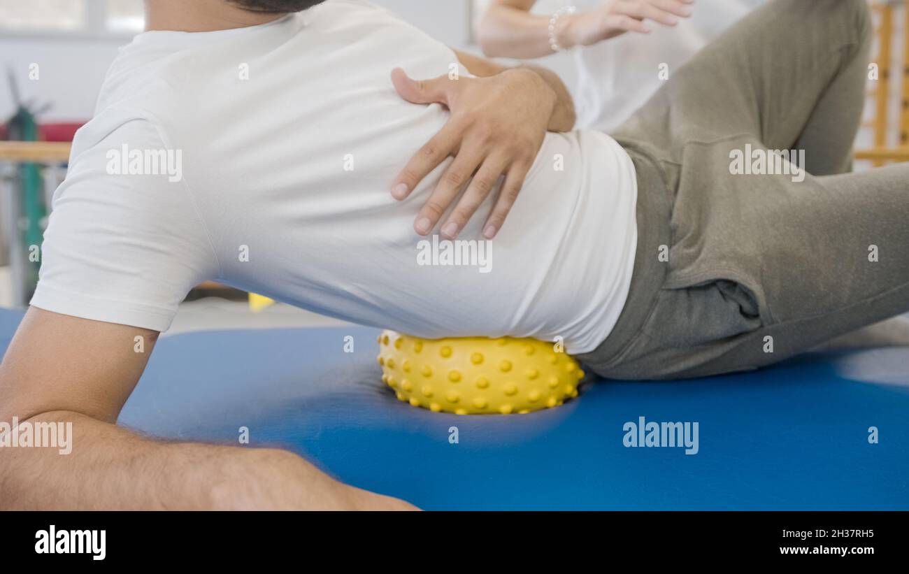Man using a spiky massage ball to release tight hips. Laying on the ball under the right hip