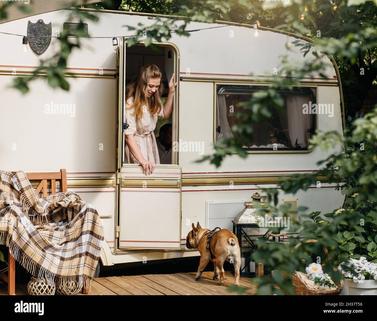 Camping and travelling . Happy person relaxing outdoors near trailer. Woman with dog is ready for road trip, Cozy sunny morning Stock Photo