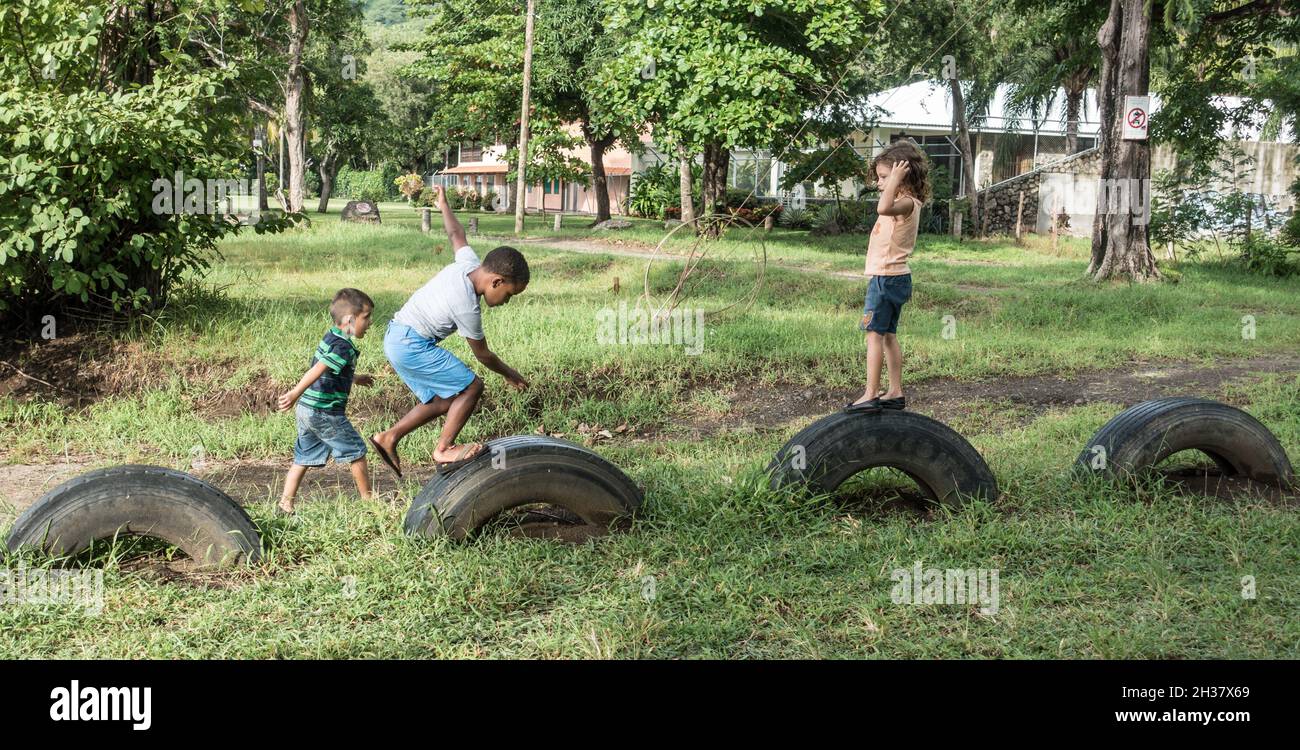 Three kids playing on old truck tires in Playa del Coco, Costa Rica. Stock Photo