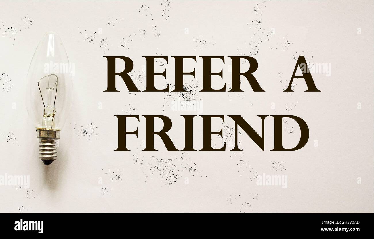 Refer a friend text written on vintage surface, next to light bulb. Referral marketing concept. Stock Photo