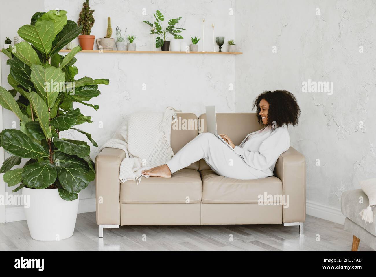 Smiling African American woman with laptop on couch. Stock Photo