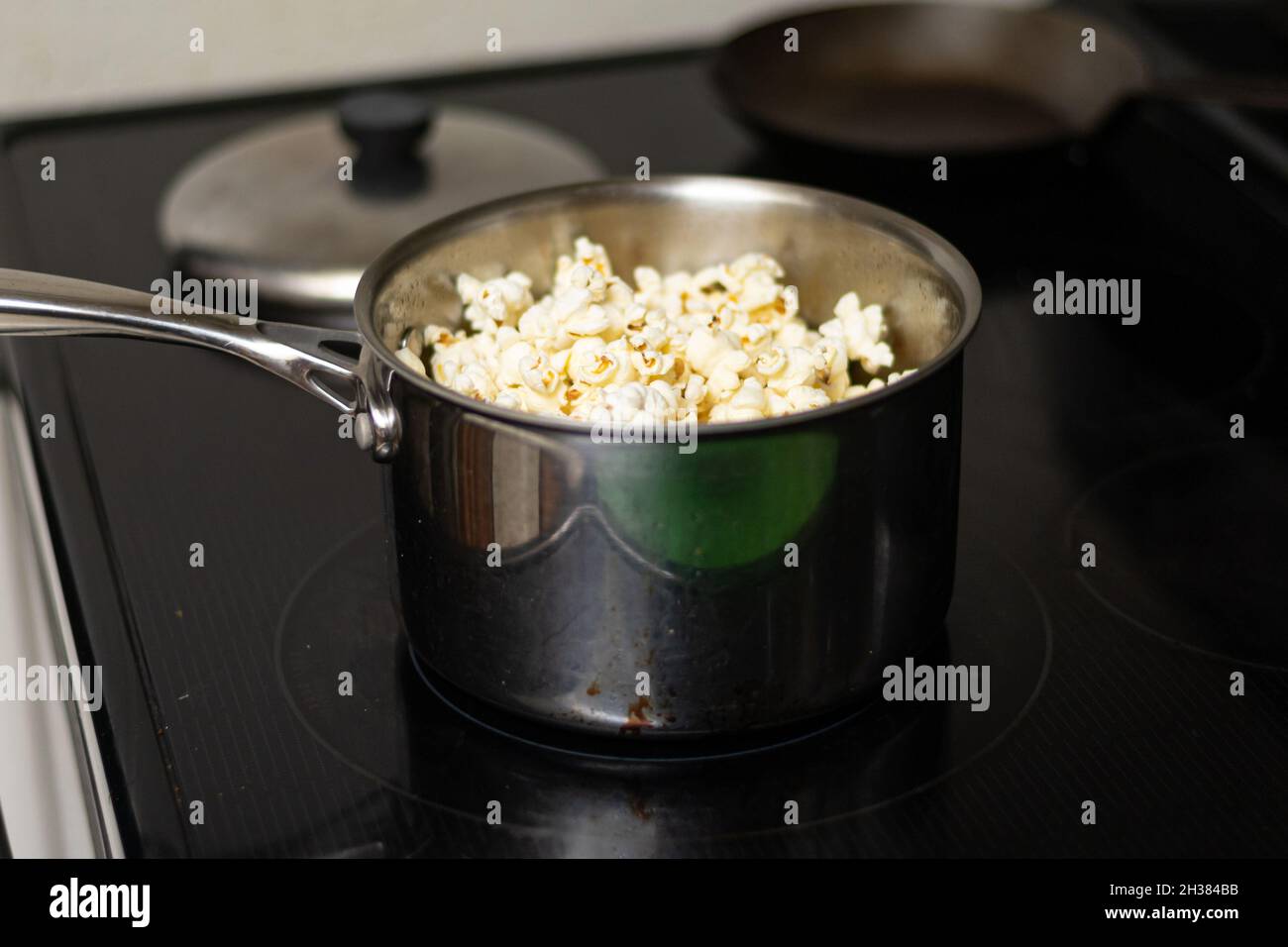A pot sits on stove with fresh hot popcorn prepared at home Stock Photo