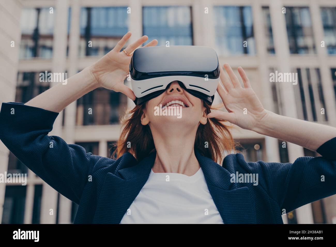 Immersed woman looking up in virtual reality while wearing portable VR, standing on city street Stock Photo