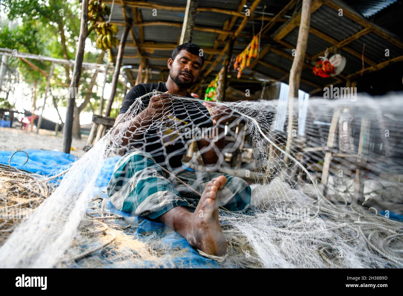 Patuakhali, Bangladesh. 22nd Oct, 2021. A fisherman is seen repairing his fishing net at Kuakata beach in Patuakhali District.Kuakata, locally known as Sagar Kannya (daughter of the sea) is located in the southwest of Bangladesh. The water level has risen due climate change and sedimentation on the sea-bed. As such tidal surges often flood the beach. The embankment, planted with various species of trees and garden, eco-park, and houses, are on the verge of extinction as erosion has taken a serious turn due to the monsoon. (Credit Image: © Piyas Biswas/SOPA Images via ZUMA Press Wire) Stock Photo