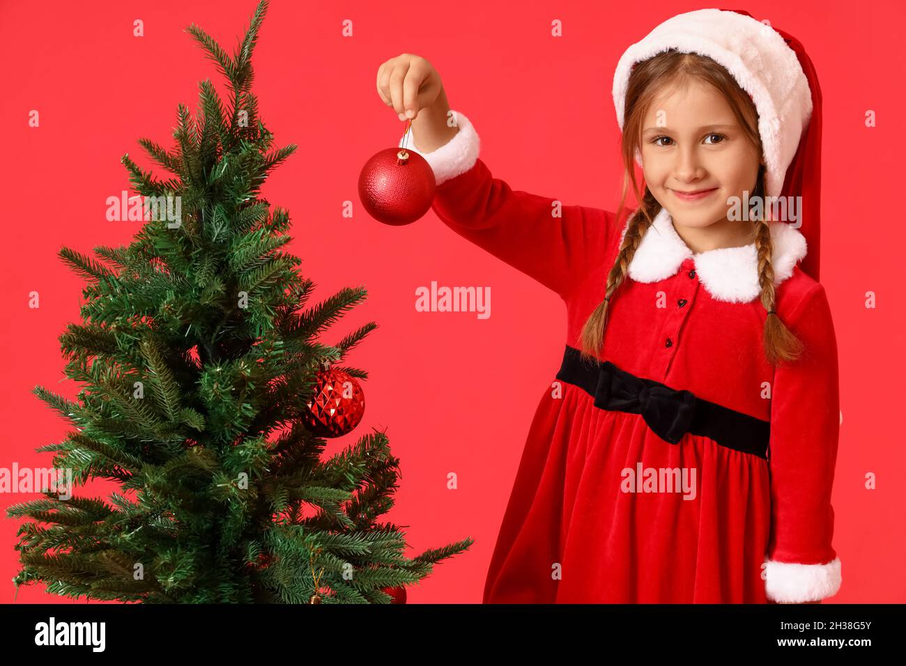 Dectrorting Little Tree Cute little girl decorating Christmas tree on red background Stock ...