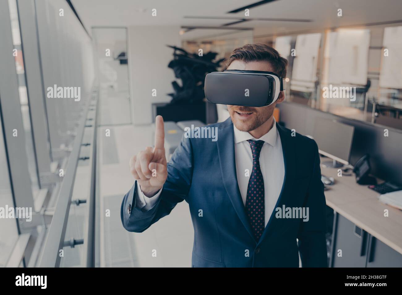 Young businessman in elegant suit using VR headset, touching exploring virtual reality at work Stock Photo