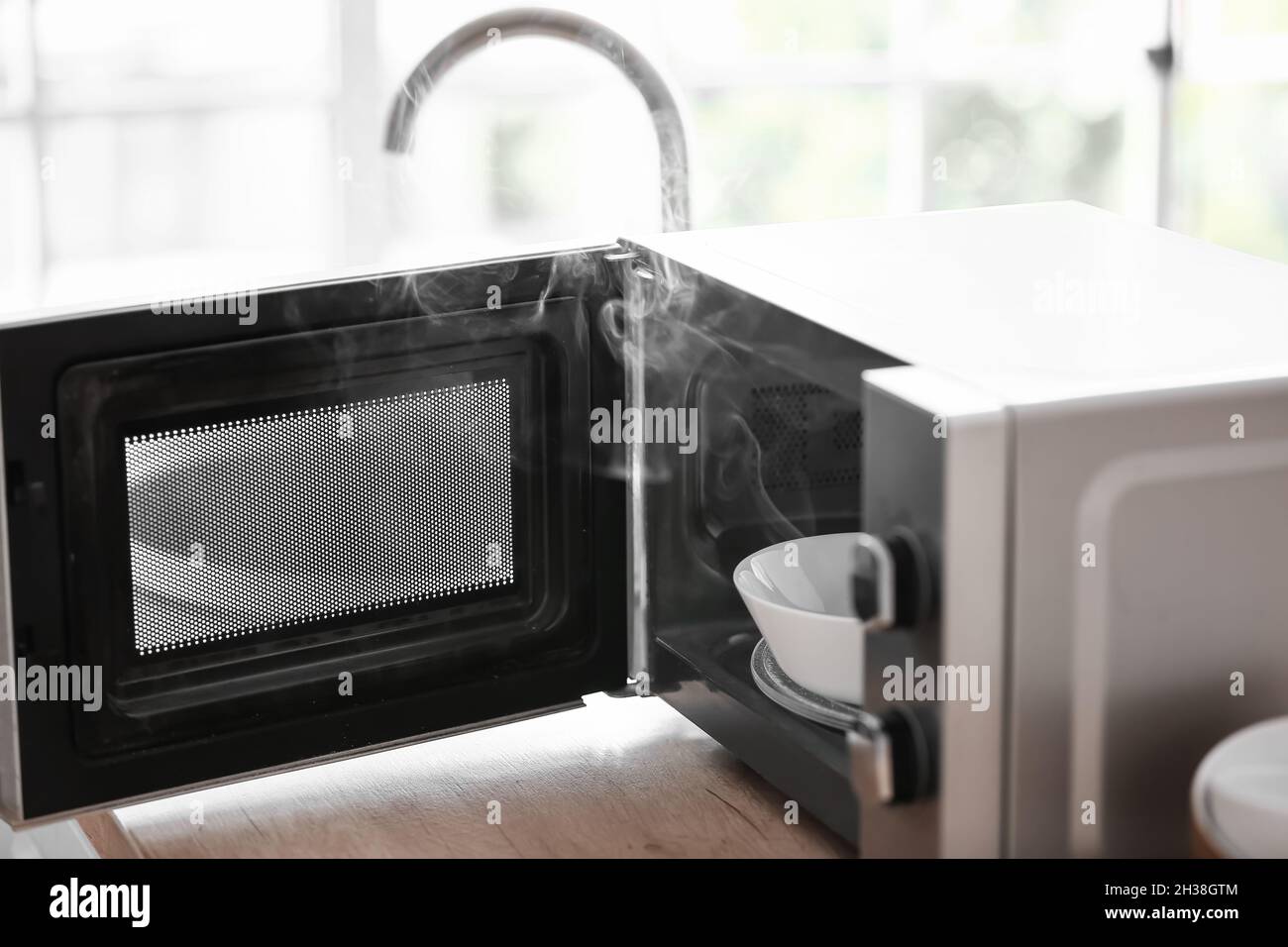 Damaged microwave oven with smoke on table in kitchen, closeup Stock