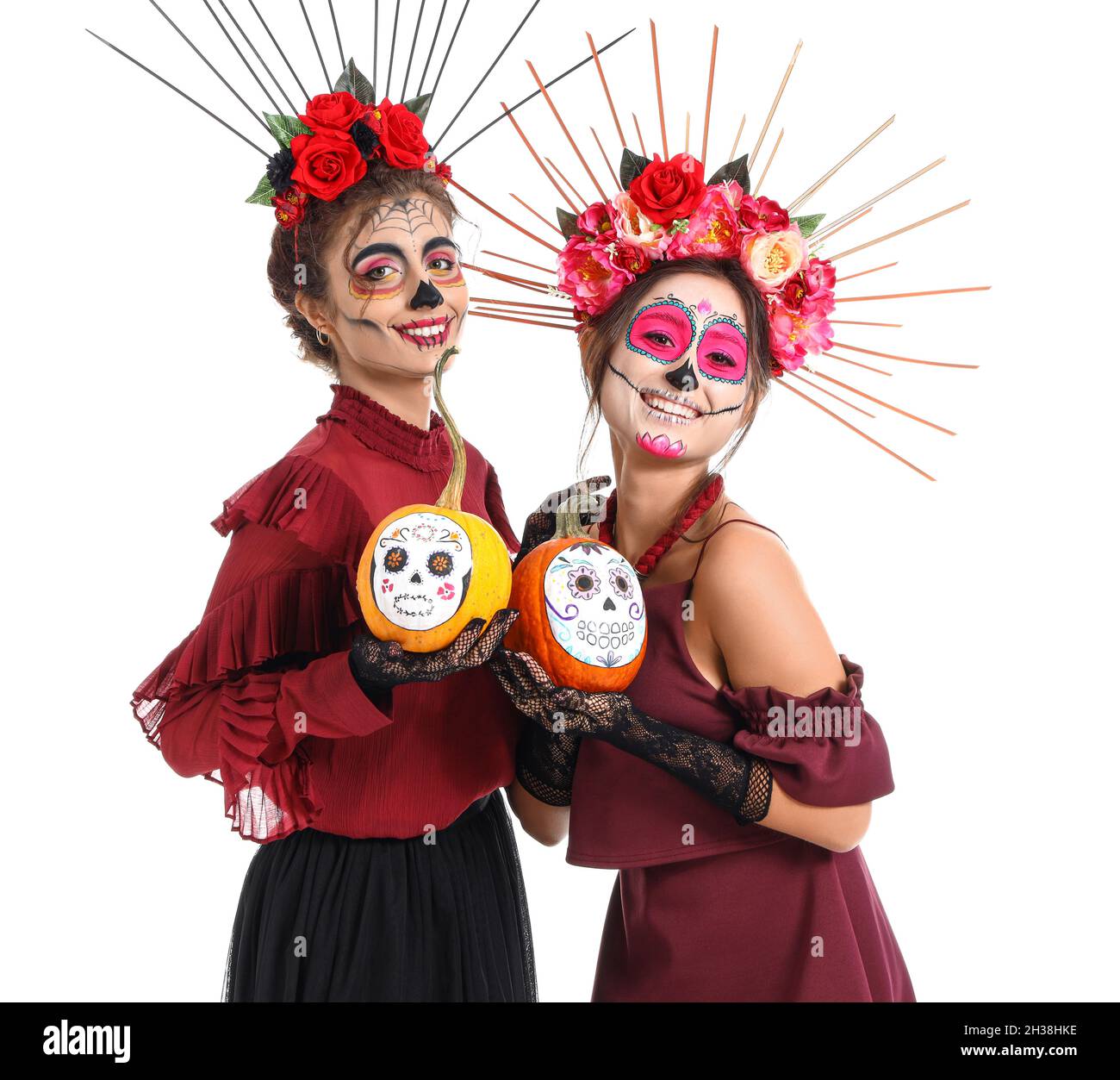 Stylish women with painted skull on faces and pumpkins against white background. Celebration of Mexico's Day of the Dead (El Dia de Muertos) Stock Photo