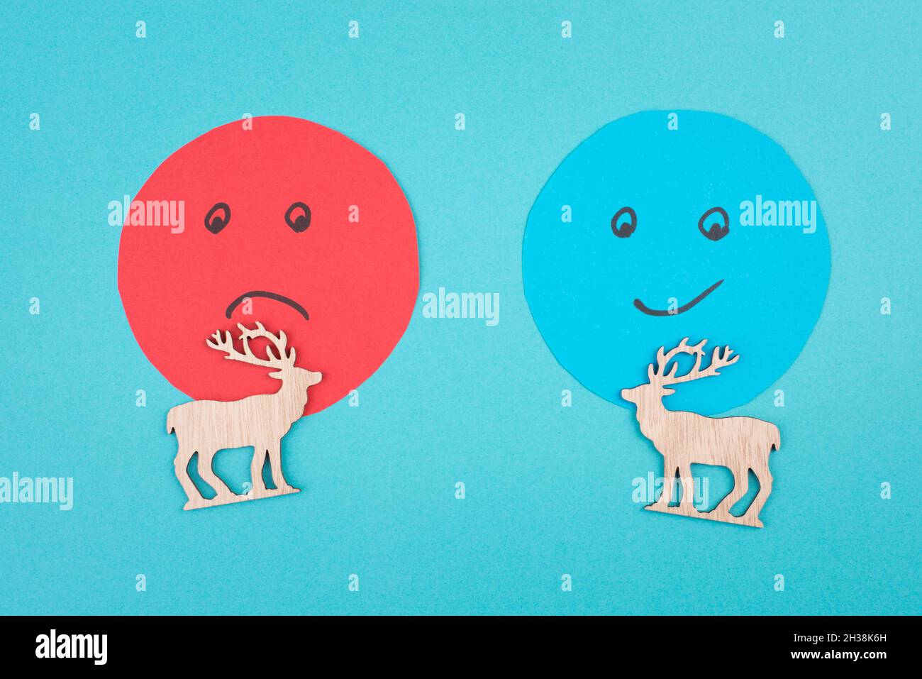 An angry and a smiling face behind two reindeers, customer rating, christmas season, concept, blue background Stock Photo