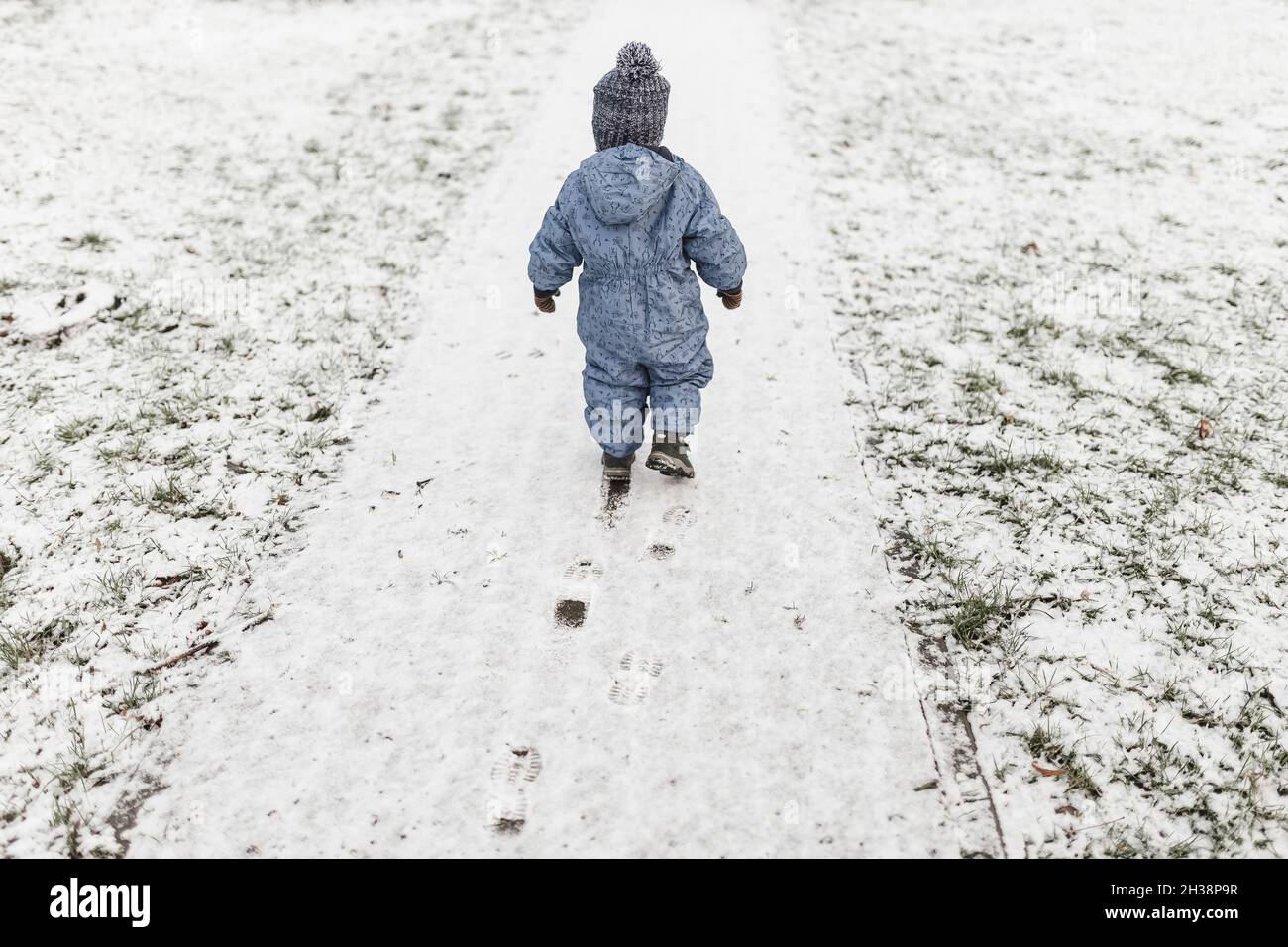 Little boy in blue onesie and warm hat walking on a snow Stock Photo