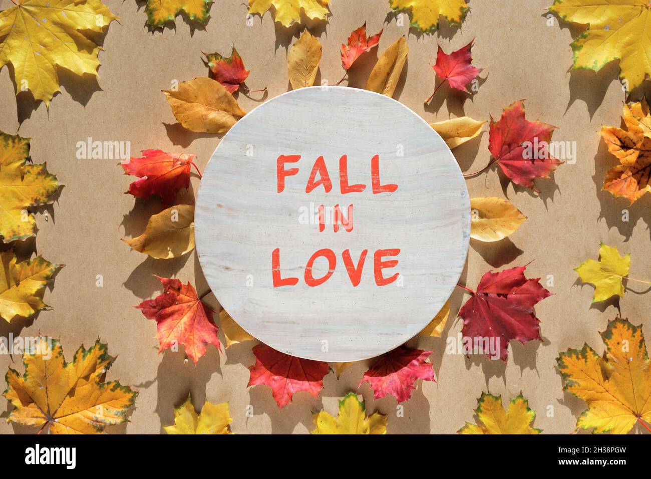 Round autumn frame made with natural Fall leaves, yellow and bright vibrant red. Maple leaves around stone board. Text Fall in Love. Creative Stock Photo