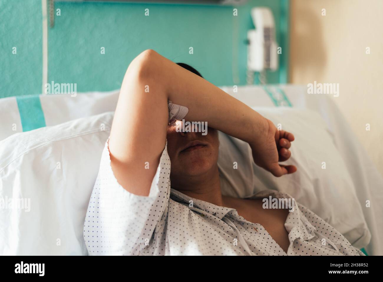 Young woman hospitalized in a bed. Gesture of pain and concern. Stock Photo