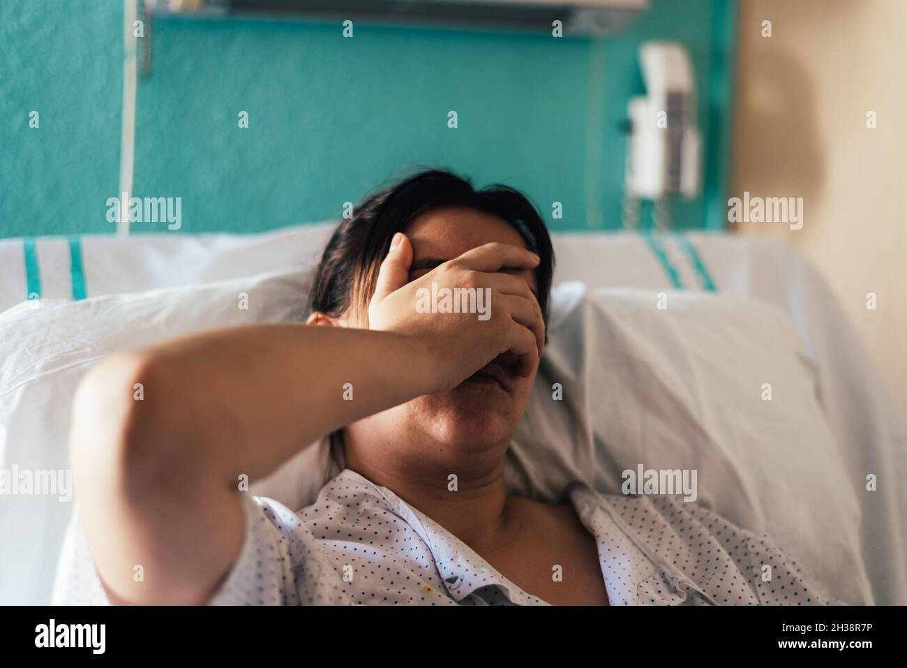 Young woman hospitalized in a bed. Gestures of pain and concern. Stock Photo