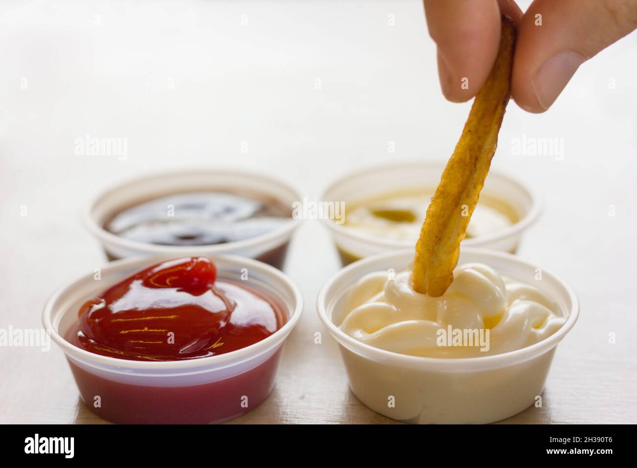 Close up on french fries dipping in mayonnaise with fingers next to