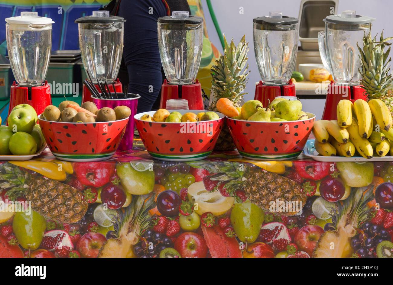 Five fruit juice makers lined up on market stand with bowls full of