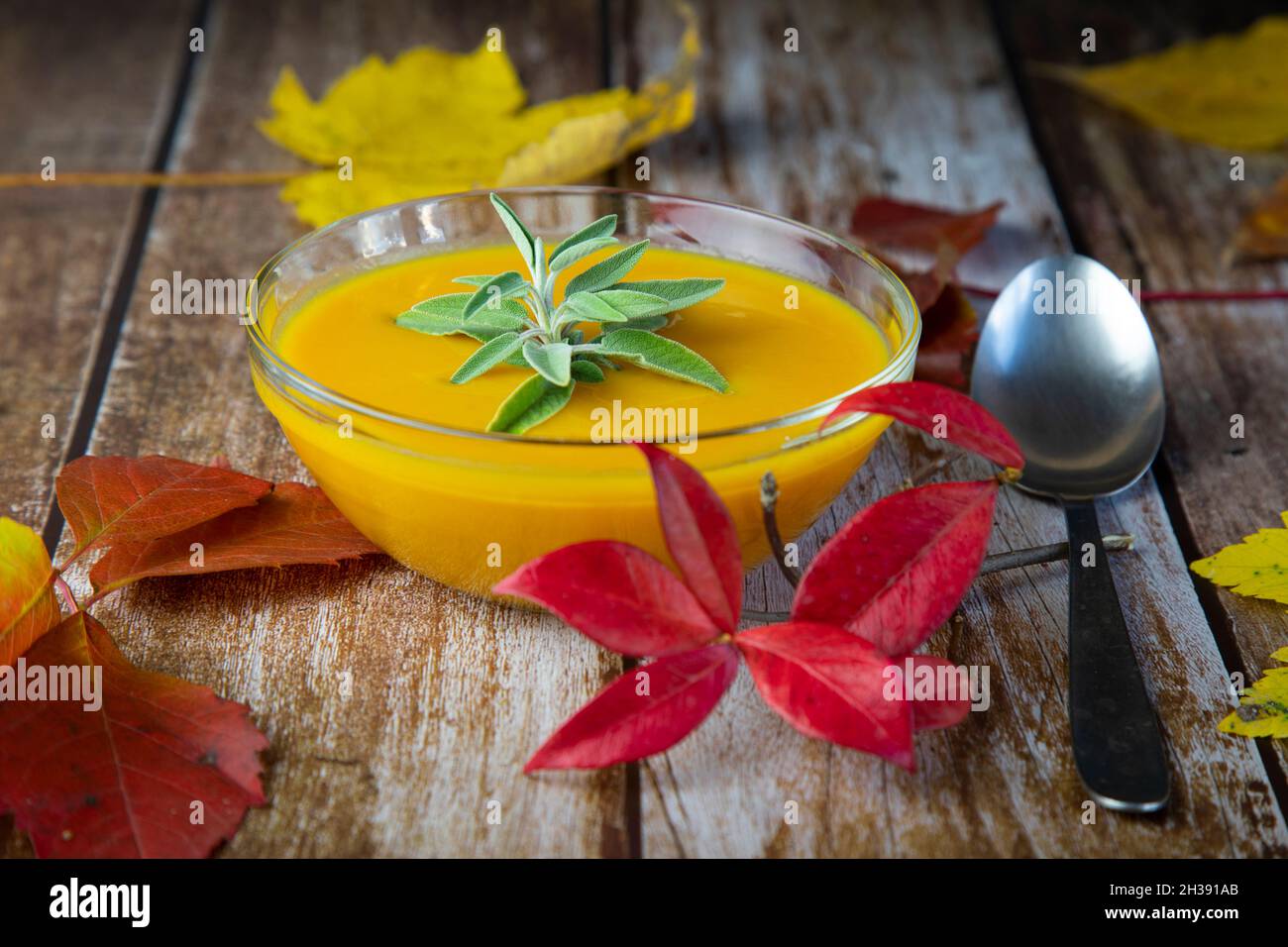pumpkin soup in a glass bowl on a wooden table decorated with autumn colorful leaves Stock Photo