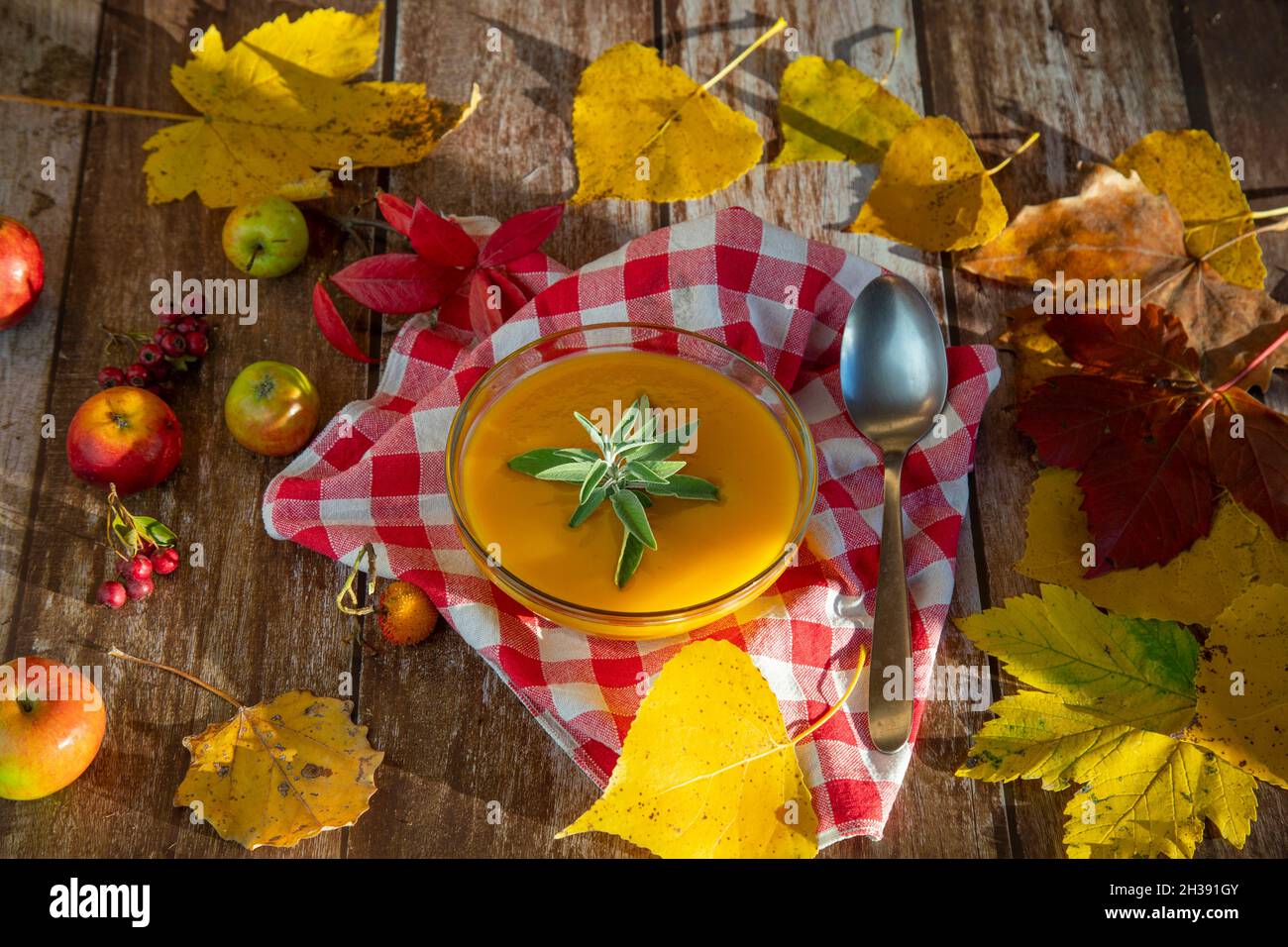 pumpkin soup in a glass bowl on a wooden table decorated with autumn colorful leaves and small wild apples Stock Photo