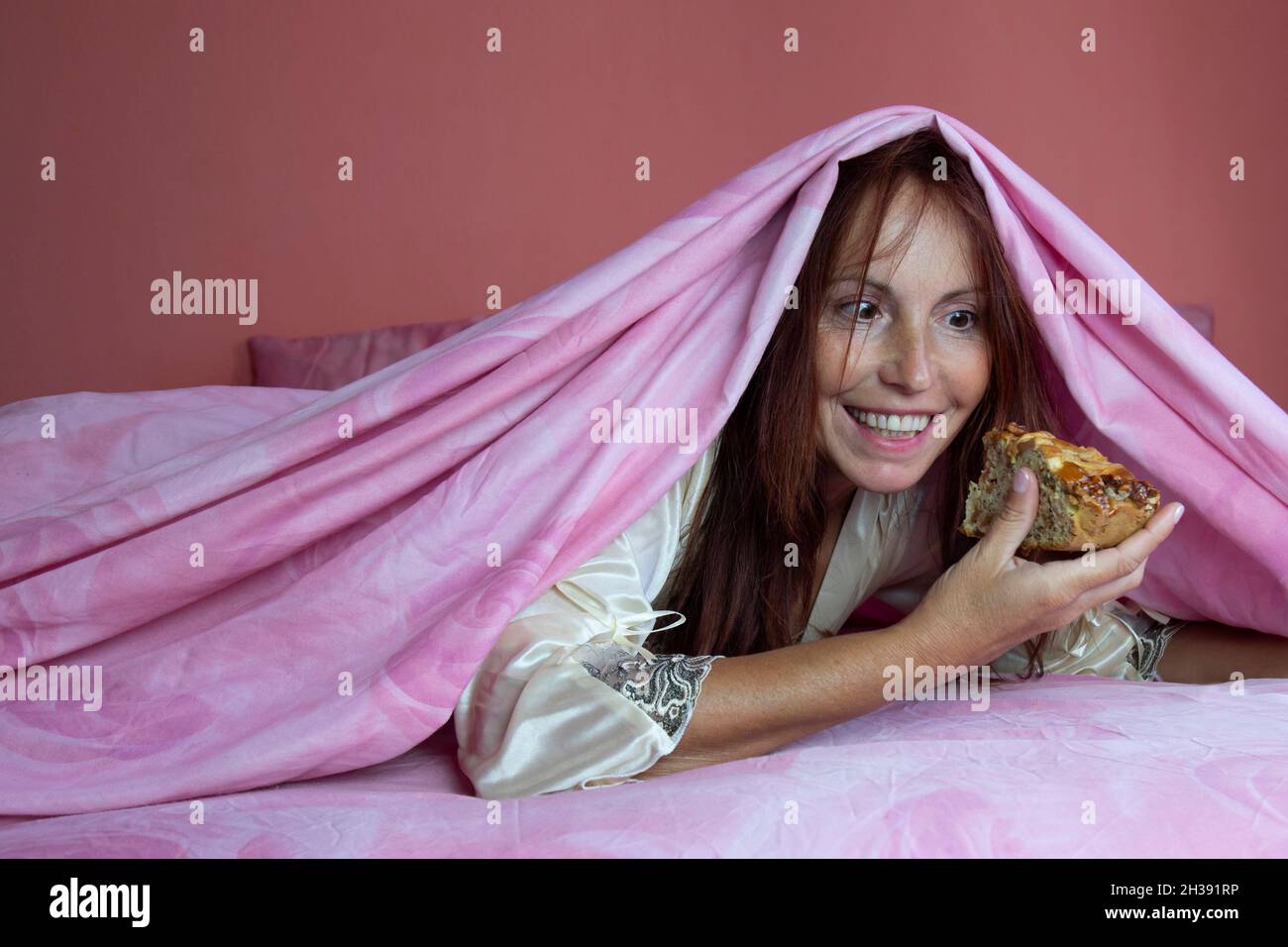 Night gluttony theme, woman on bed secretly eating a piece of pie Stock Photo
